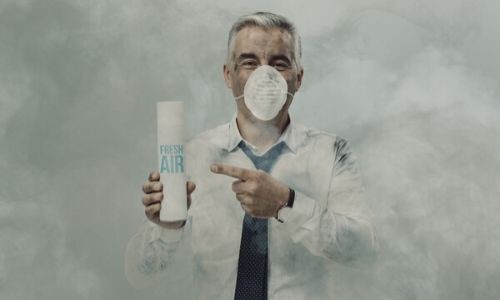 A man wearing a face mask and holding a can of fresh air in a smoky environment