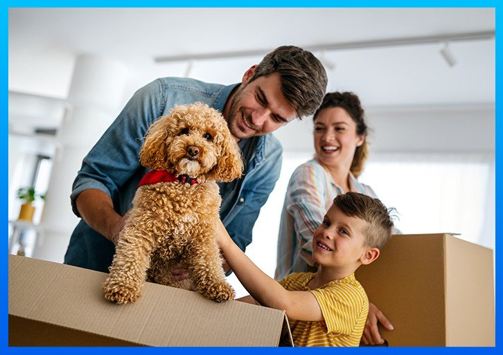 Family holding moving boxes and smiling. A smally curly dog is in the foreground